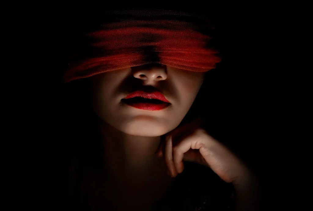Potret gelap seorang wanita dengan mata tertutup kain merah, melambangkan kebutaan terhadap realitas dan fakta akibat terlalu mempercayai gosip.