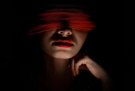 Potret gelap seorang wanita dengan mata tertutup kain merah, melambangkan kebutaan terhadap realitas dan fakta akibat terlalu mempercayai gosip.
